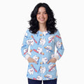 A woman modeling a light blue zip-up scrub top with a cartoon tooth pattern holding colorful toothbrushes, shown against a plain white background.
