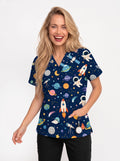 A smiling blonde woman wearing a navy blue V-neck scrub top with a colorful space-themed print of rockets, astronauts, planets, and stars, paired with black pants, against a plain white background.