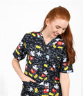 Female healthcare worker wearing black cartoon mouse printed medical scrub top with front pockets.
