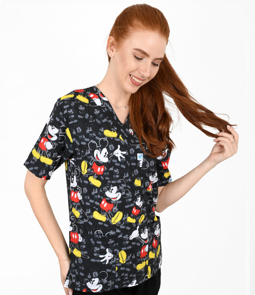 Woman wearing a black scrub top with colorful Mickey Mouse pattern on a white background