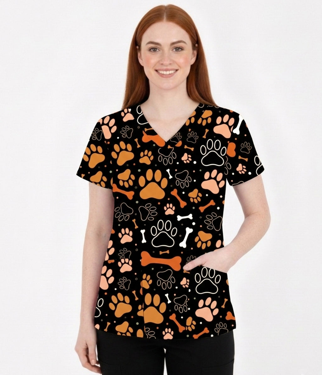Female model wearing Paws & Bones veterinary scrub top with paw print and bone pattern on black background.